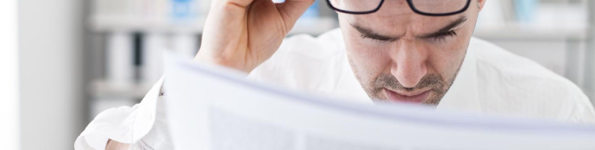 Homme lisant un journal en tenant ses lunettes de vu sur son front